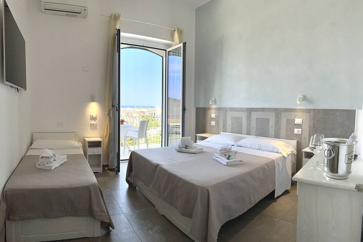 Habitación de hotel con dos camas individuales, un balcón con mesa y sillas, un minibar y vistas a la ciudad.