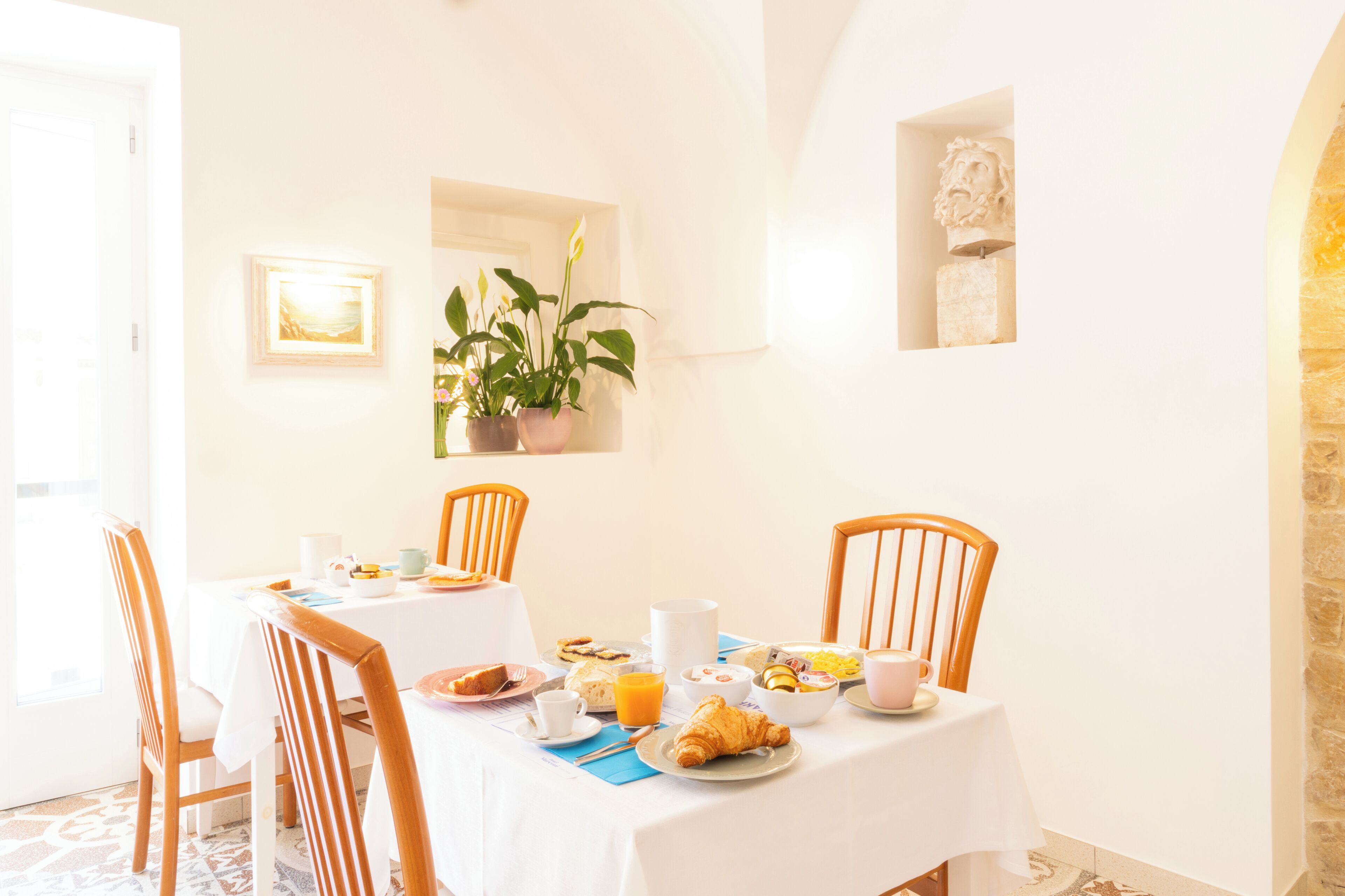 A breakfast table set with plates, cups, and a croissant, surrounded by wooden chairs.