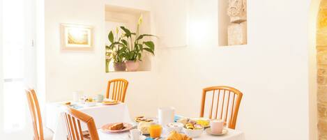A breakfast table set with plates, cups, and a croissant, surrounded by wooden chairs.