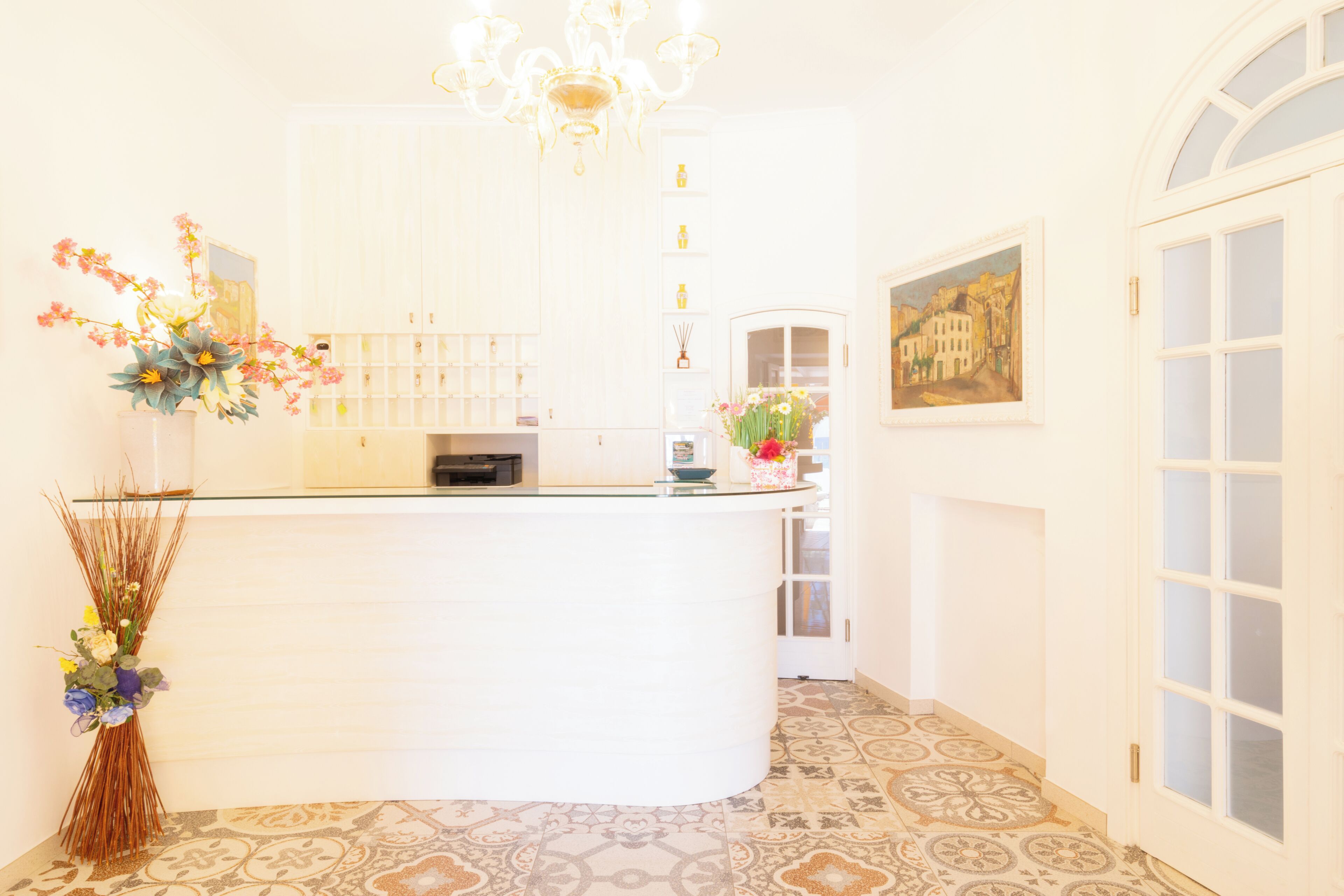 A reception area with a curved counter, a chandelier, a painting on the wall, and a patterned floor.