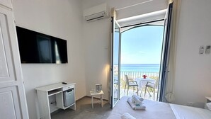 A hotel room with a bed, a desk, a TV, a balcony with a table and chairs, and a view of the sea. - Hotel Marconi (Sperlonga)