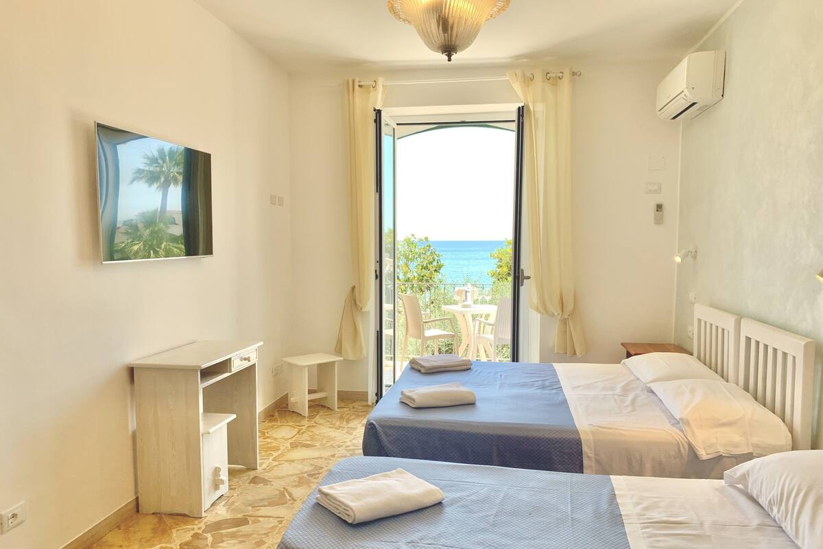Habitación de hotel con dos camas, un escritorio, una silla, una mesita y vista al mar.