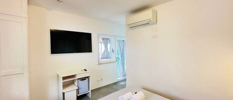 A hotel room with a bed, a desk, a television, an air conditioning unit, and a window with curtains.