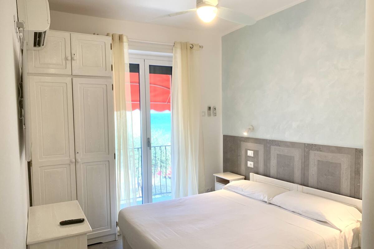 Un dormitorio con cama, mesita de noche, armario y balcón con vistas.