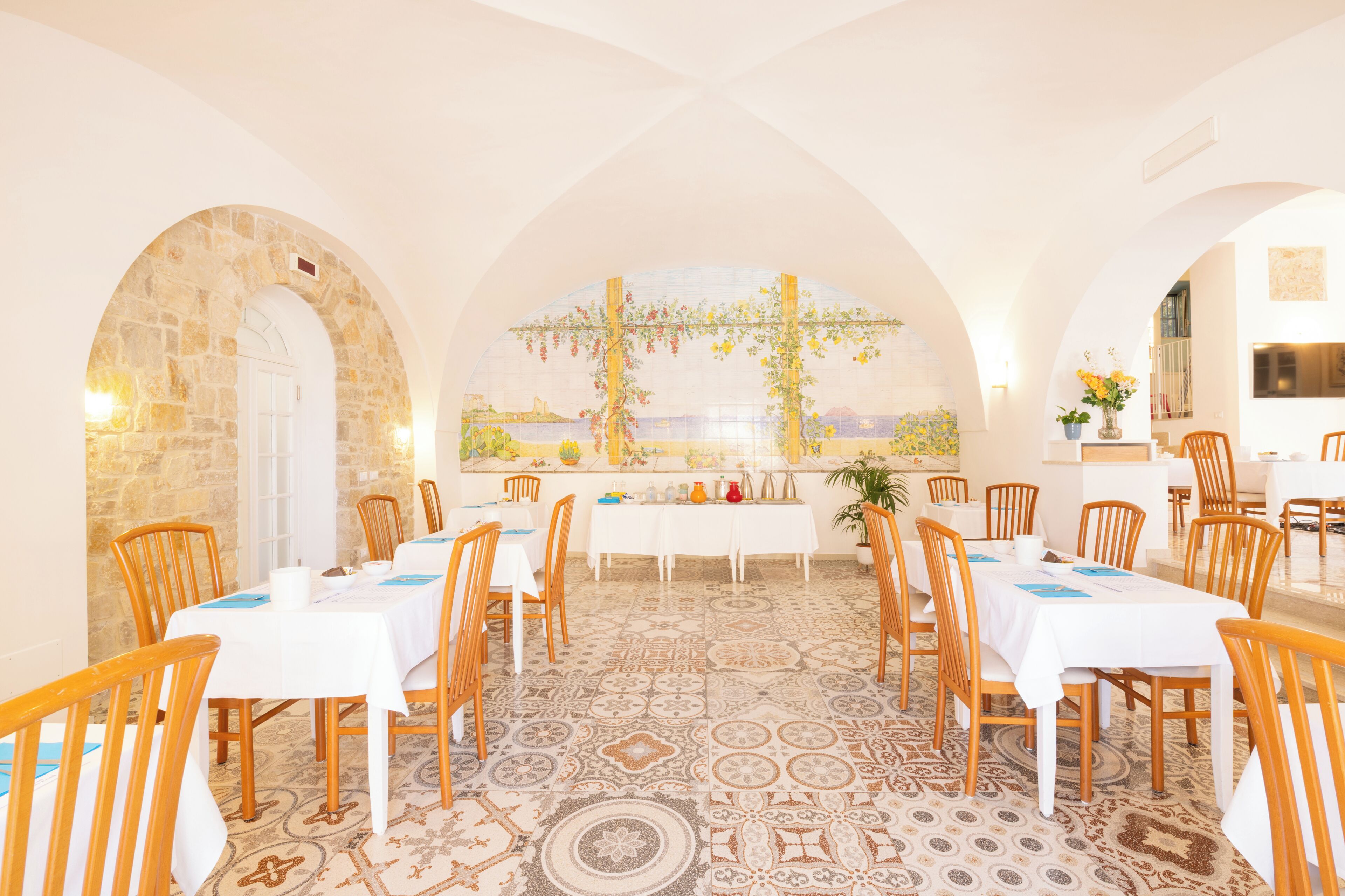 Un área de comedor con mesas y sillas, una pared de piedra y vistas a través de una ventana.