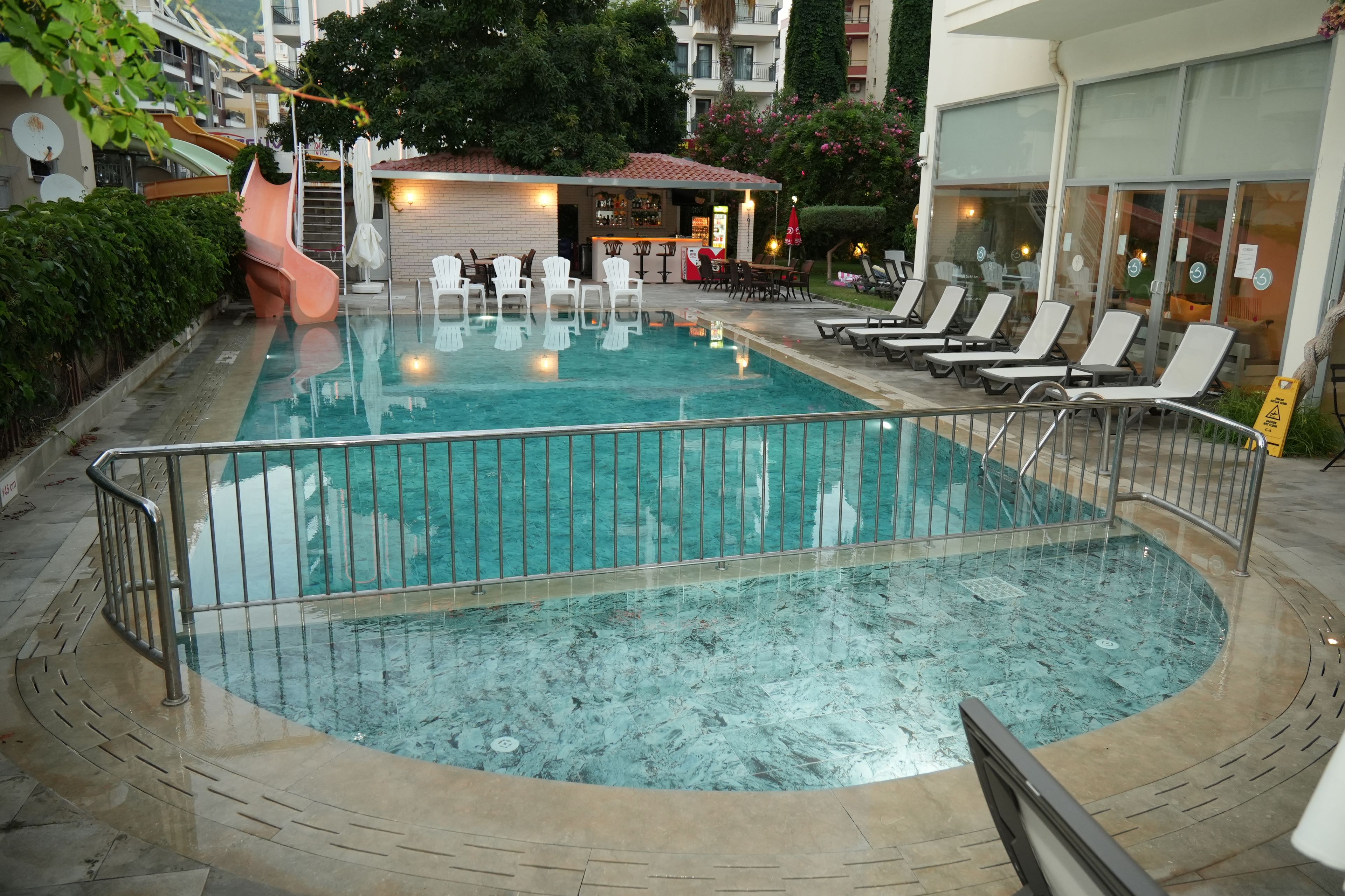 Ein Schwimmbecken mit einer umlaufenden Sonnenterrasse, Liegestühlen und einer Bar.