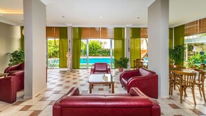 Eine großzügige Lobby mit roten Ledersofas, einem Couchtisch und Holzstühlen. Durch große Fenster ist ein Pool zu sehen.