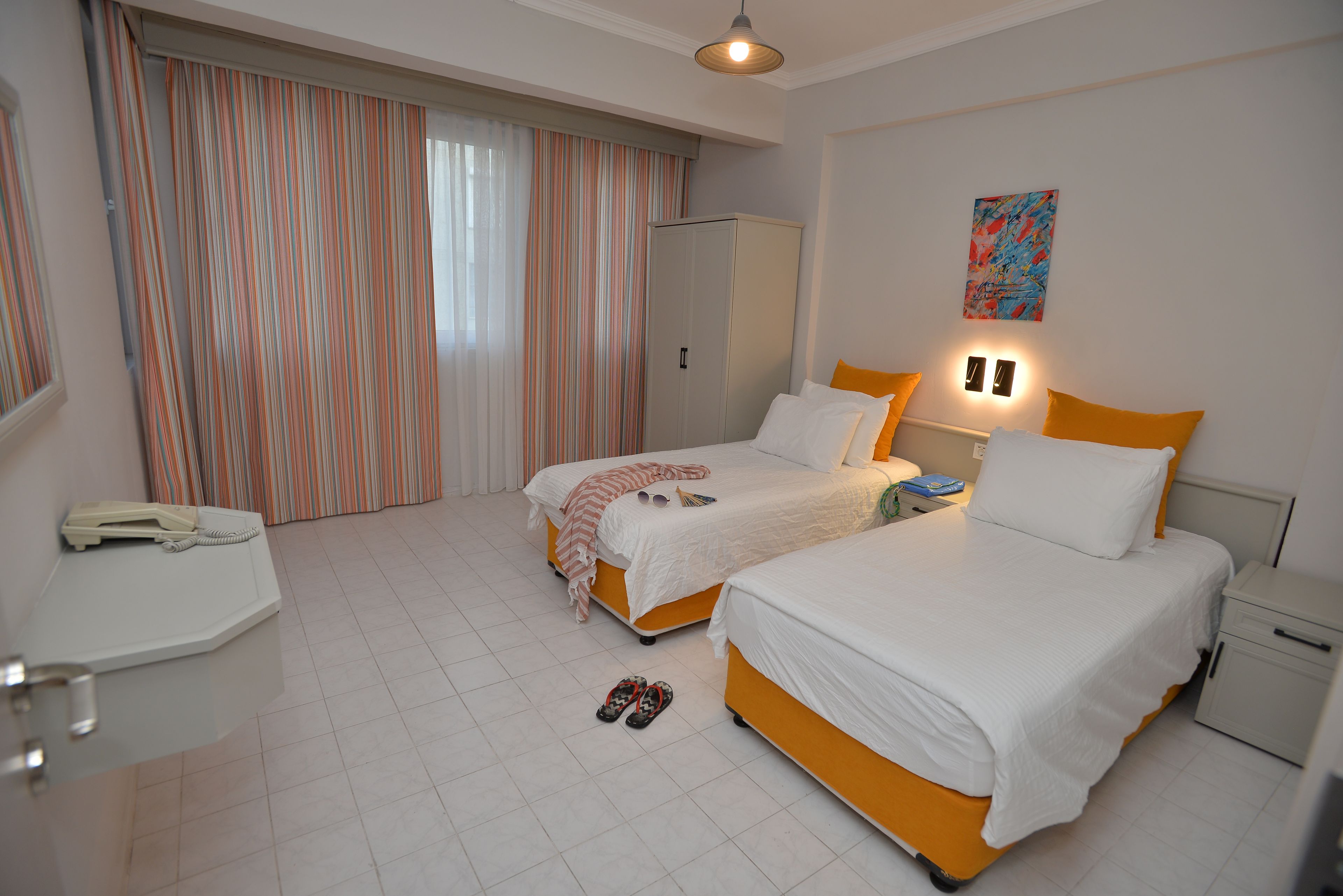 A hotel room with two beds, a desk, a telephone, and a window with curtains.
