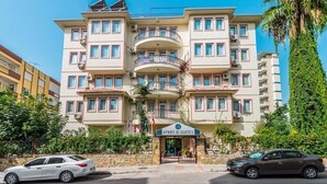 Ein mehrstöckiges Hotel mit Balkonen, einem Schild mit der Aufschrift "APART & SUITES" und parkenden Autos davor.