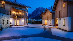 A snow-covered courtyard with wooden buildings, a stone wall, and a mountain in the background. - Liondes Chalets (Marebbe)