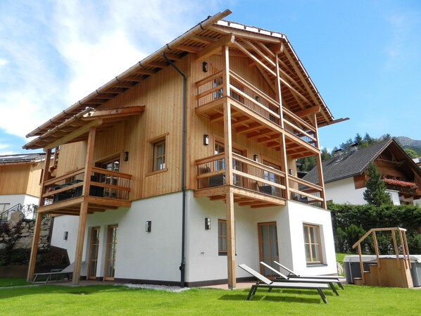 A multi-story wooden chalet with balconies, a stone foundation, and a well-maintained lawn.