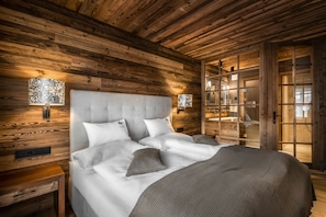 A wooden-paneled bedroom with a large bed, two bedside lamps, and a wooden nightstand. - Liondes Chalets (Marebbe)
