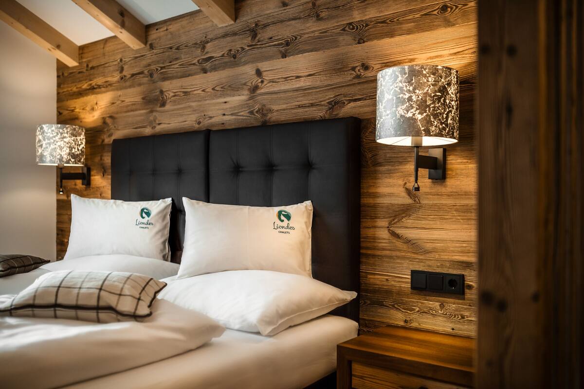 Une chambre à coucher avec une tête de lit sombre, deux oreillers blancs ornés d’un logo et deux lampes murales à l’aspect marbré.