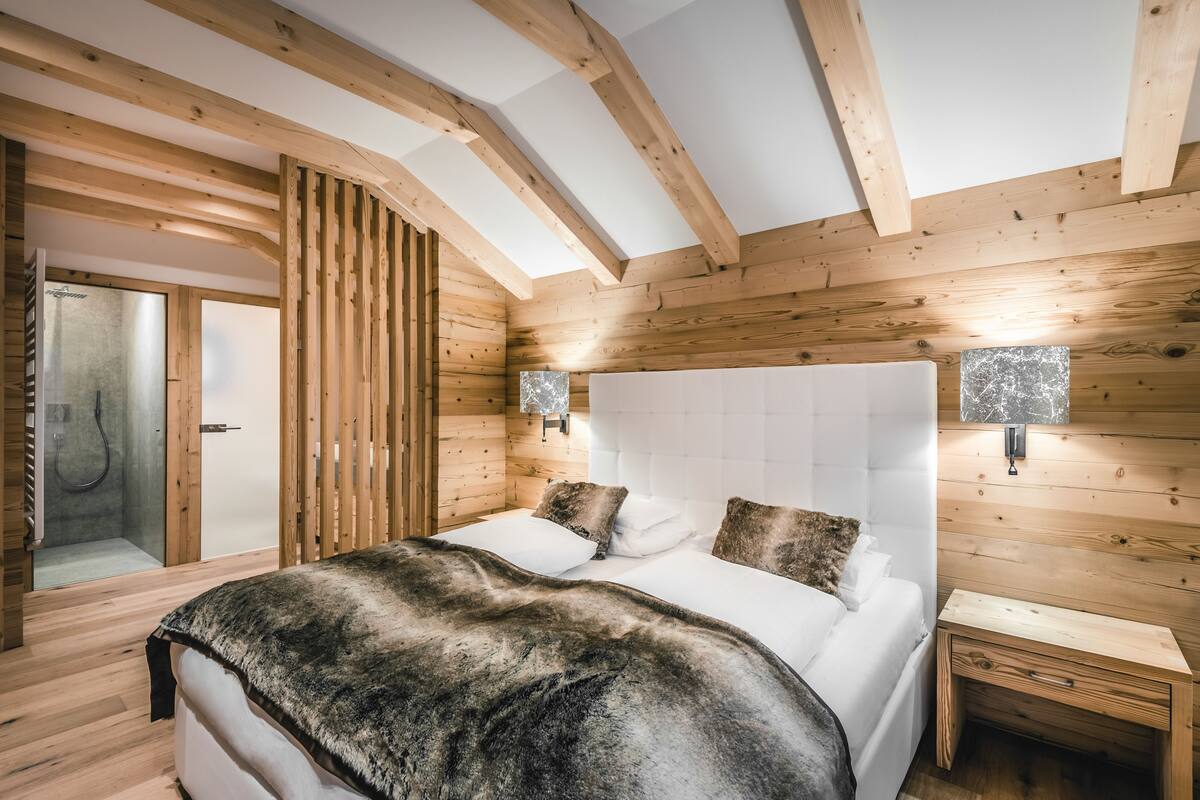 Une chambre aux murs lambrissés, comprenant un lit, des tables de chevet et une cabine de douche en verre.