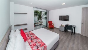 Una habitación de hotel moderna con una cama grande, un escritorio, una silla, un televisor y un ventanal corredero al exterior.