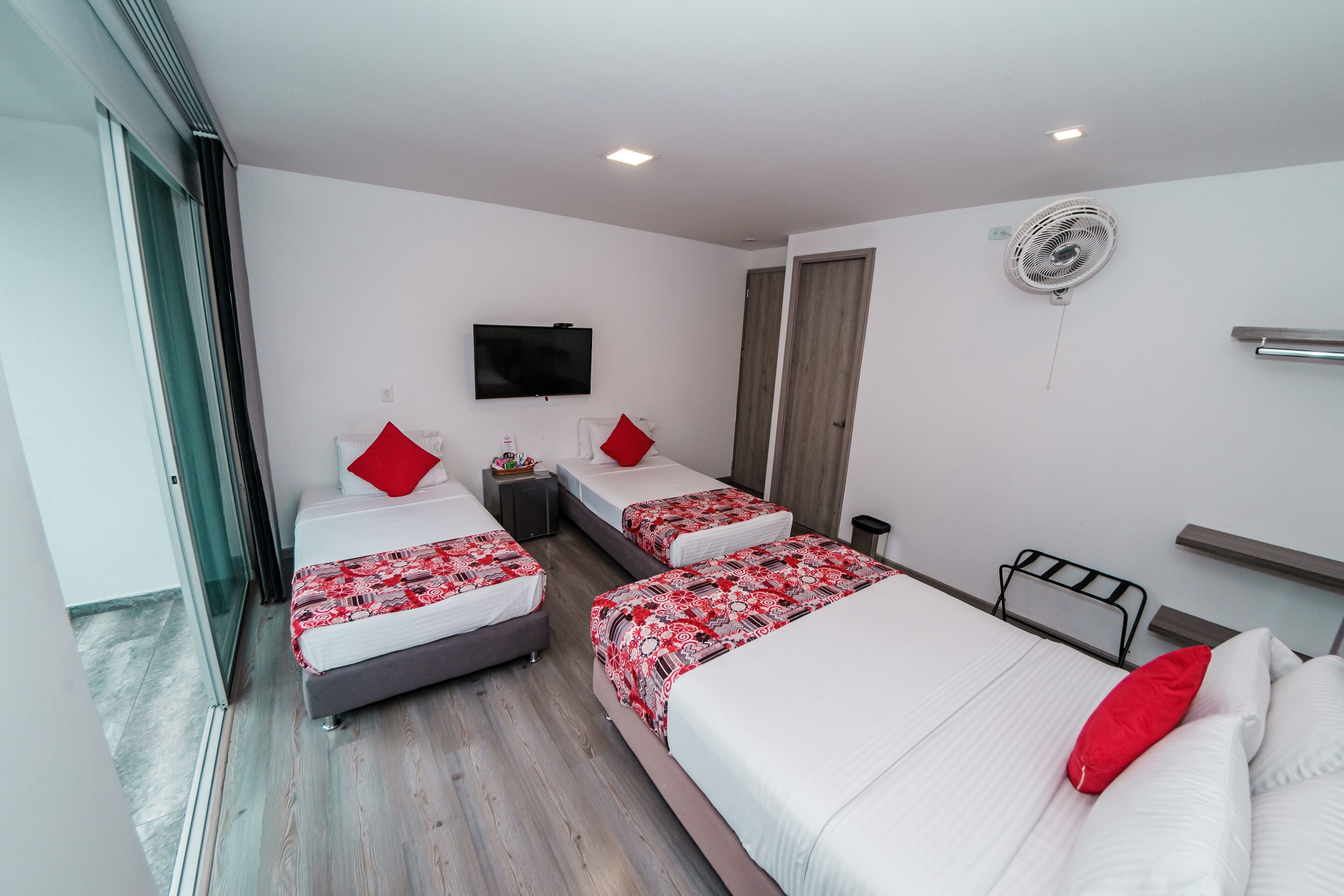 A hotel room with three beds, a TV, a fan, and a sliding door.