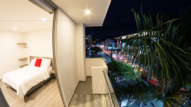 Un dormitorio moderno con cama, mesitas de noche y vista a un paisaje urbano nocturno.
