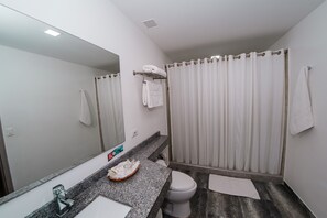 Un baño moderno con encimera de granito, un lavabo blanco, un inodoro y una cortina de ducha.
