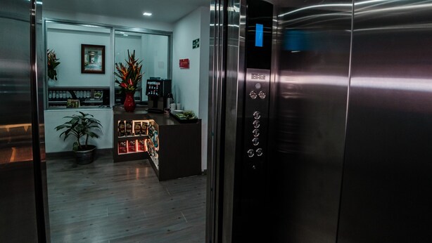 An elevator interior with a control panel, a reception desk, and a potted plant. - Hotel Portal Del Norte Armenia (Armenia)