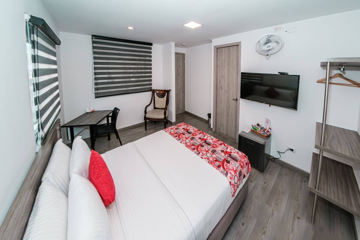 A hotel room with a bed, a desk, a chair, a TV, and a wardrobe.