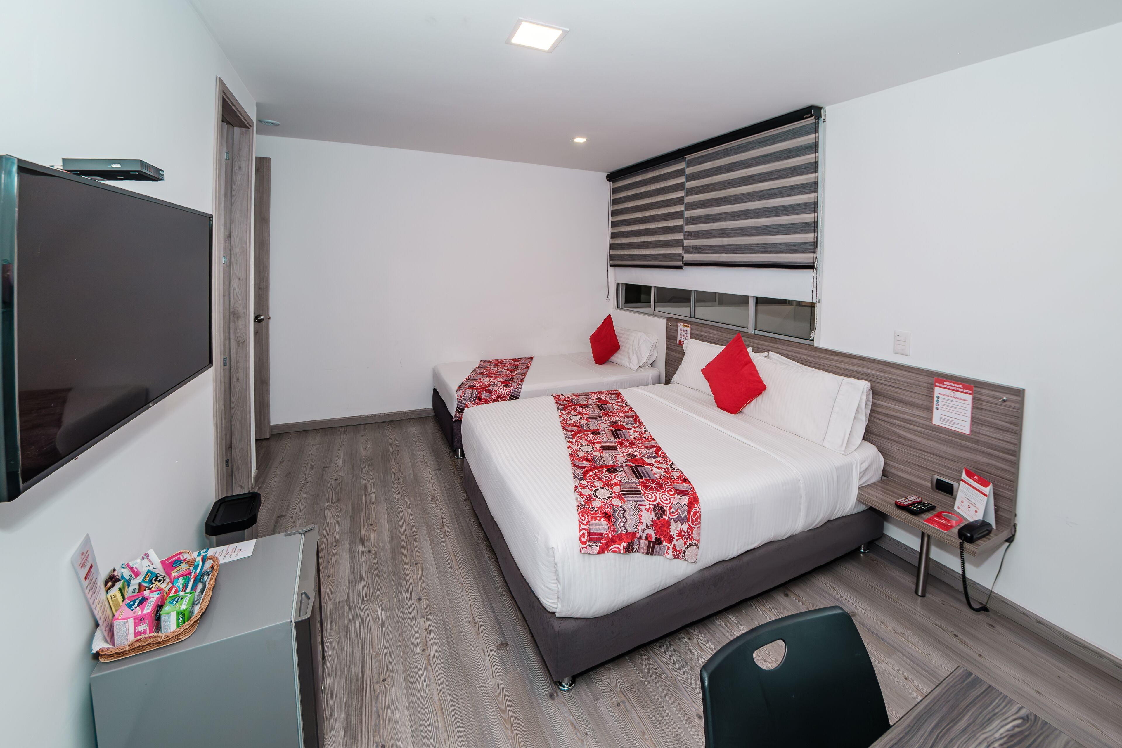 A modern hotel room with a large bed, bedside tables, a flat-screen TV, and a window with blinds.
