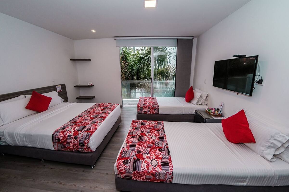 A hotel room with three beds, a TV, and a balcony with a view of palm trees.