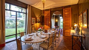 A dining area with a round table set for six, surrounded by chairs, with a view of a garden through large windows. - Villa avec piscine privée et Golf (Marrakech)