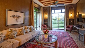 A spacious living room with a sofa, a coffee table, and a TV. There are large windows and a ceiling fan. - Villa avec piscine privée et Golf (Marrakech)