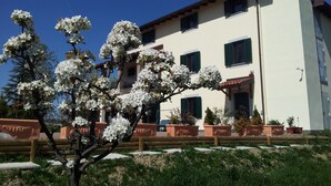 Un edificio con varias ventanas y balcones, rodeado de árboles floreados y plantas en macetas.