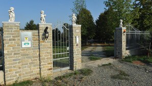 Una entrada protegida por una reja, con pilares de piedra, estatuas y un medidor de gas.