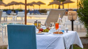 Une table dressée pour le petit-déjeuner, avec vue sur le coucher de soleil au-dessus de la piscine.