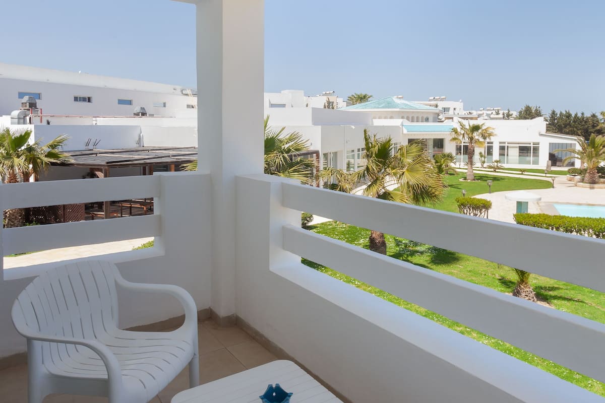 A balcony with white chairs and a table, overlooking a pool and buildings.