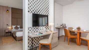 Una habitación de hotel moderna con una cama, un escritorio con silla, un televisor y un pequeño comedor con mesa y sillas.