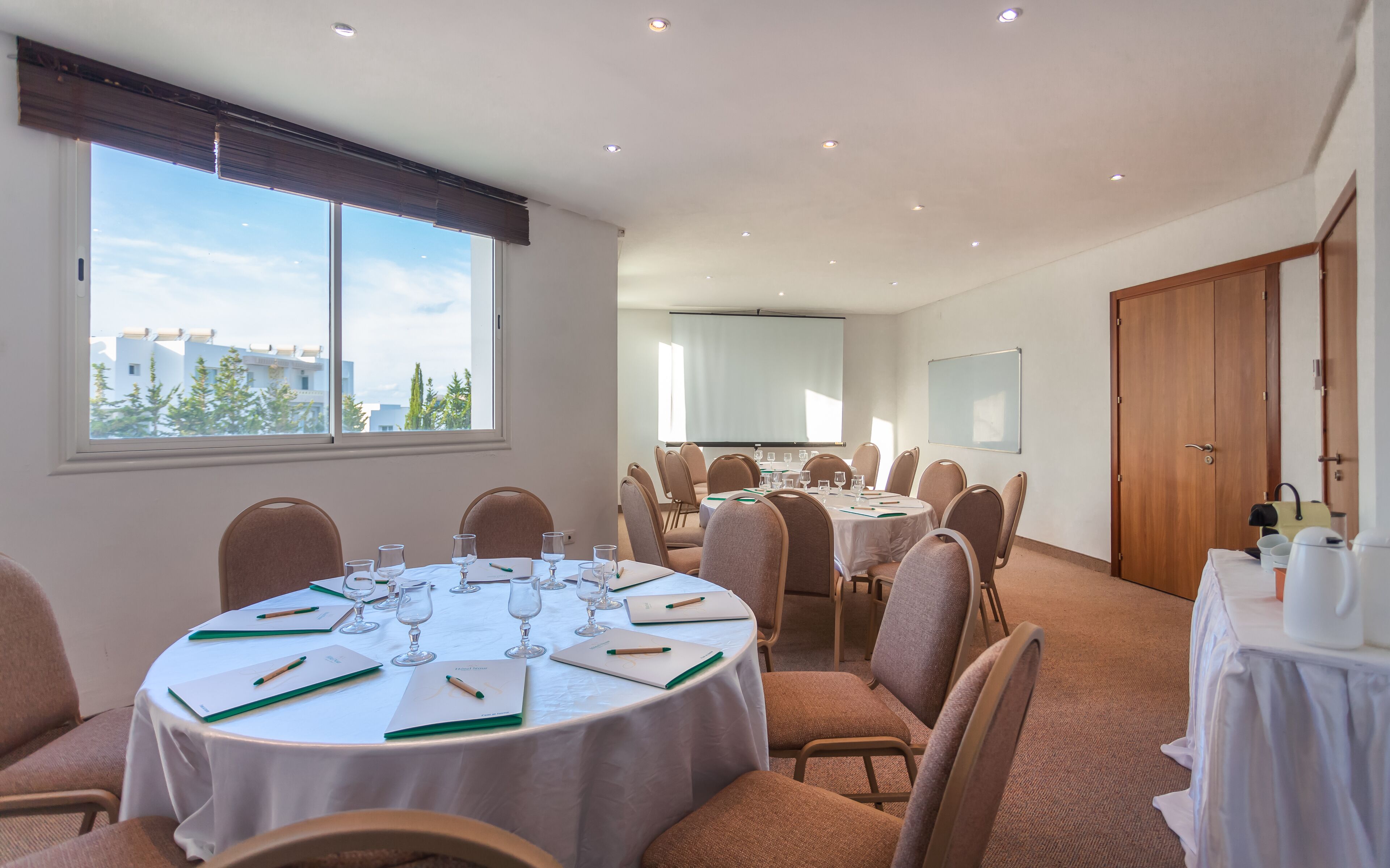A conference room with round tables, chairs, and a large window with a city view.