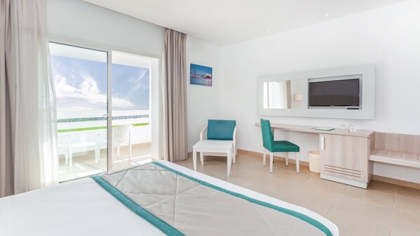 Una habitación de hotel moderna con una cama grande, un escritorio, una silla, un televisor y un balcón con vista al mar.