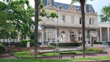 A historic building with a fountain, palm trees, and a bench in the foreground.