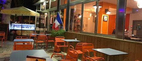 Un espace extérieur aménagé avec des chaises et des tables orange, un drapeau français et un kiosque à desserts.