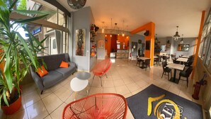 A modern interior with a grey sofa, red chairs, and a dining area with tables and chairs. - Rev Hotel (Lamalou-les-Bains)
