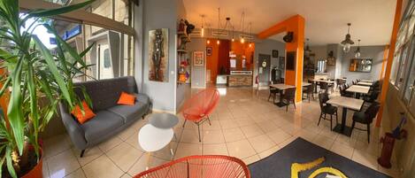 A modern interior with a grey sofa, red chairs, and a dining area with tables and chairs.