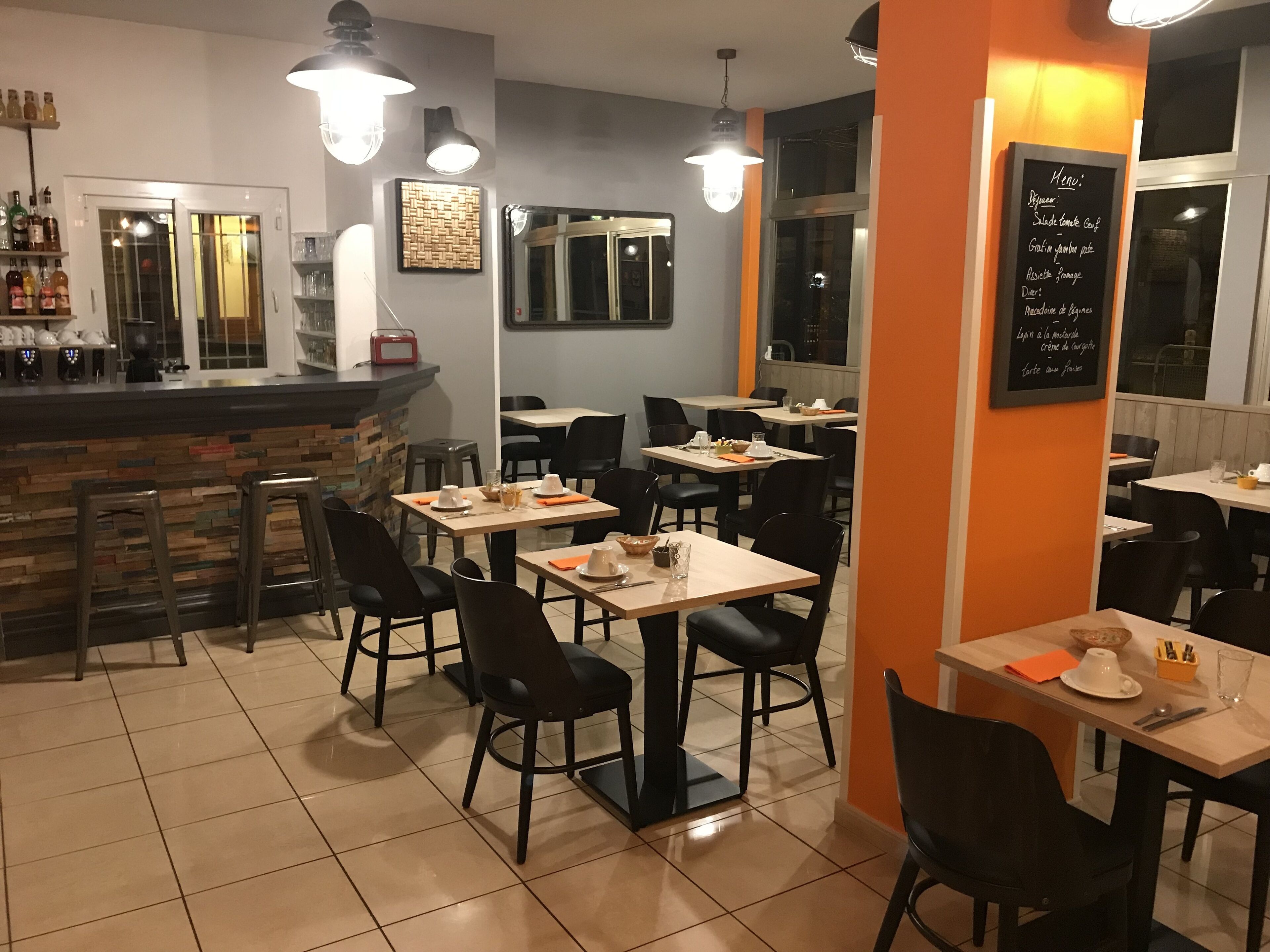 Ein Restaurantinneres mit mehreren Tischen und Stühlen, einer Bar und einer Tafel mit der Speisekarte.