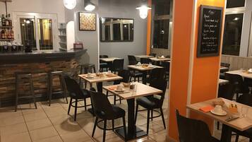 A restaurant interior with multiple tables and chairs, a bar area, and a chalkboard menu.
