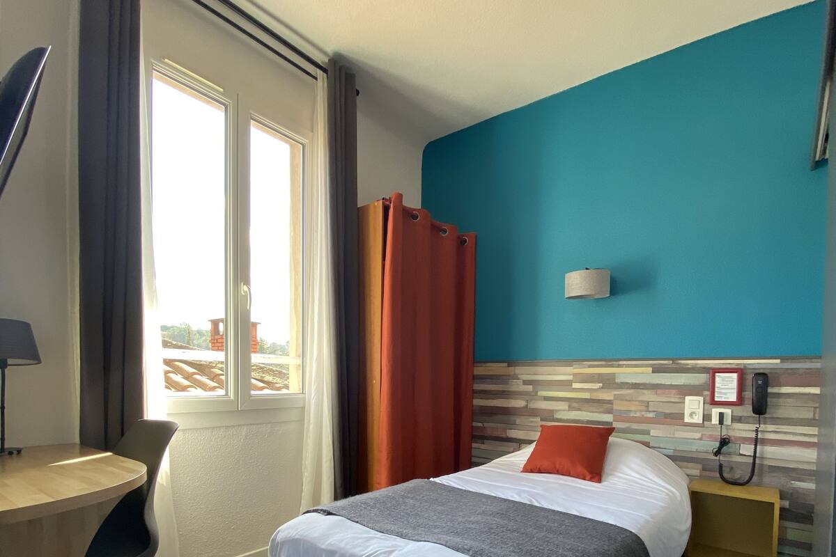 A hotel room with a bed, a desk, a chair, a nightstand, and a telephone.