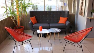 Un rincón acogedor con un sofá y dos sillones rojos, una mesita con una lámpara y una planta en maceta.