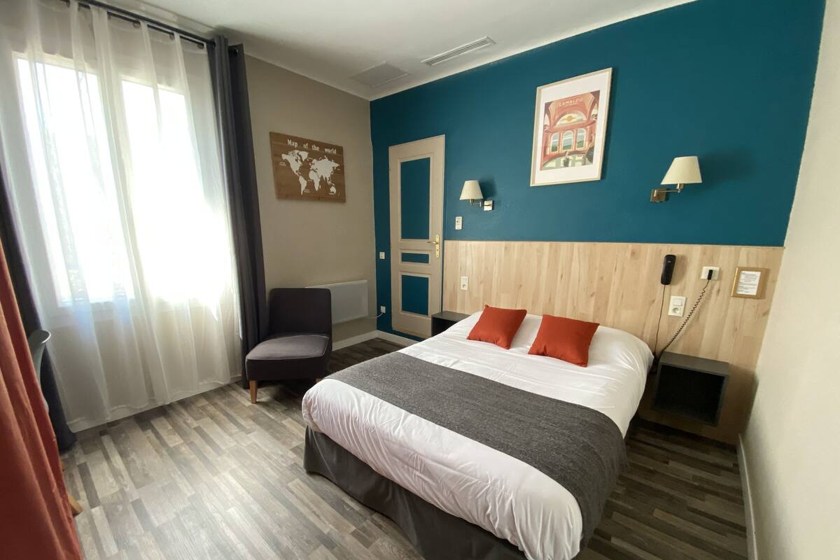 A hotel room with a bed, a chair, a map on the wall, and a door.