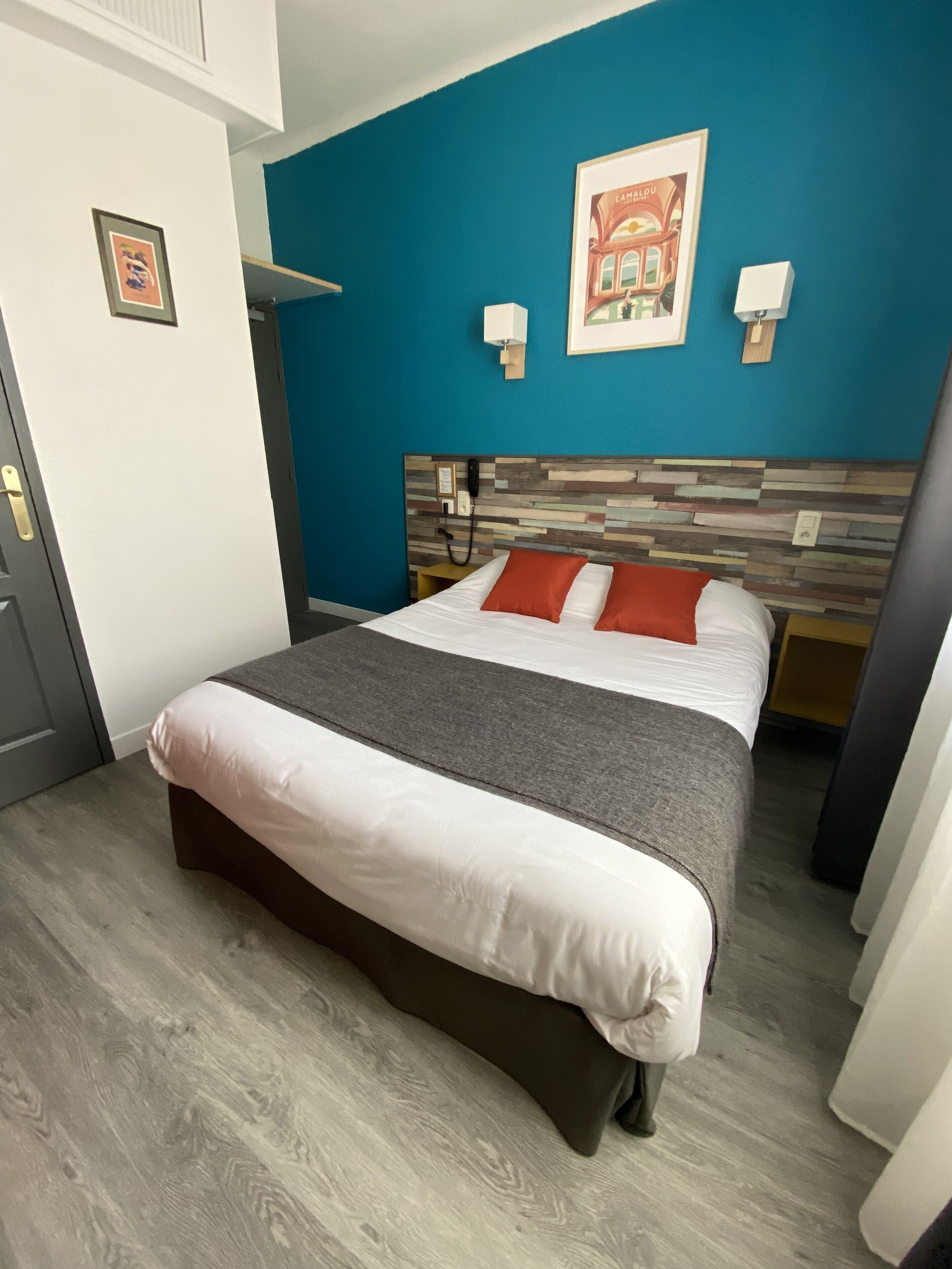 Une chambre d’hôtel avec un lit, un mur d’accent bleu, une tête de lit en bois et un tableau encadré accroché au mur.