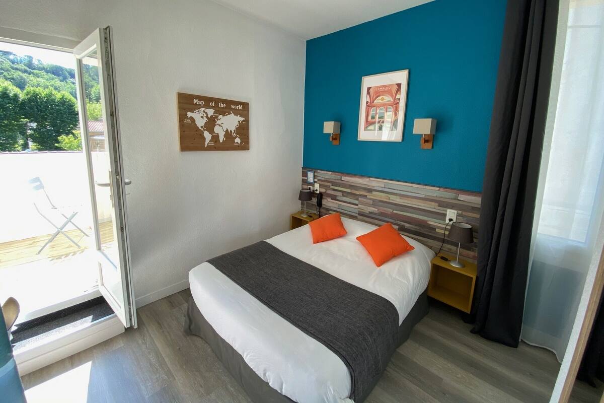 A hotel room with a bed, two pillows, a world map on the wall, a framed picture, and a view of the outdoors.