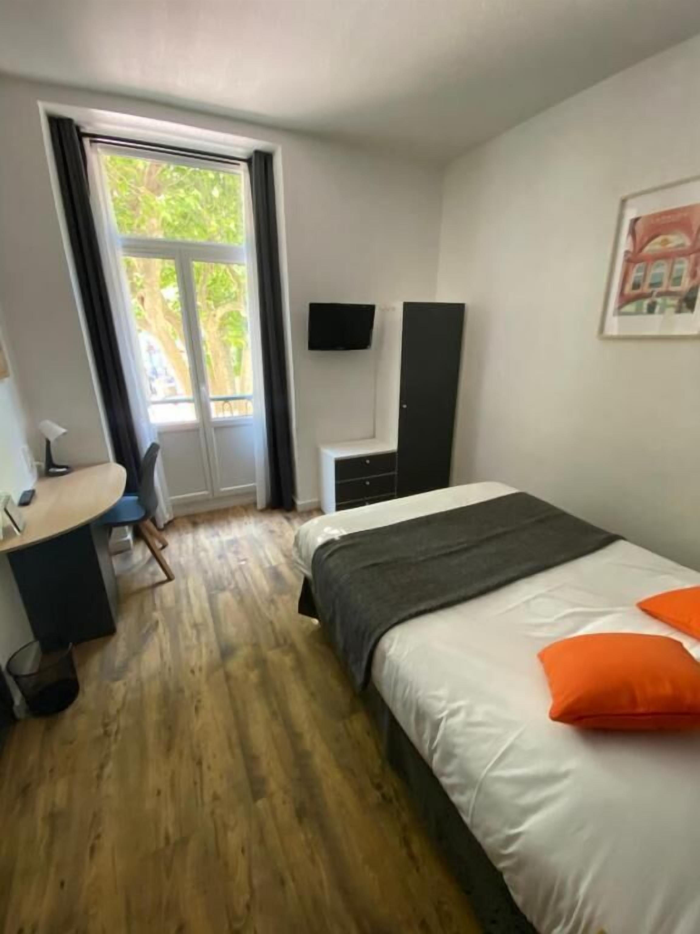 A hotel room with a bed, a desk, a chair, a TV, and a window with curtains.