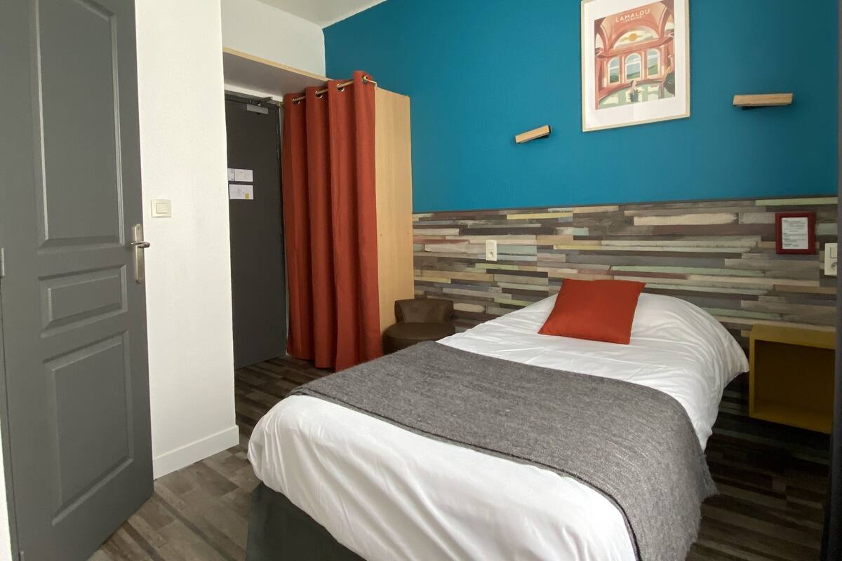 A hotel room with a bed, a nightstand, a chair, a door, and a blue wall with a picture.