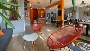 A modern dining area with high chairs, a coffee machine, and a visible kitchen area. - Rev Hotel (Lamalou-les-Bains)