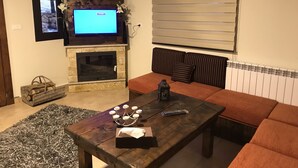 A living room with a fireplace, a television, a sofa, and a coffee table. - Villars (Mayrouba)
